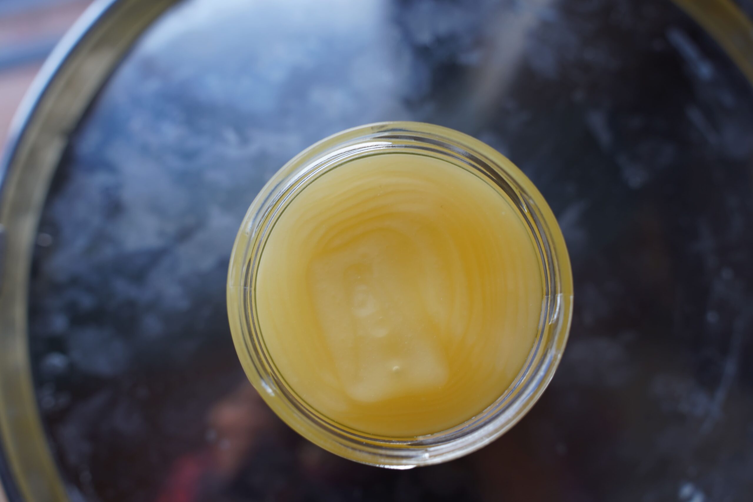 Ein mit Honig gefülltes Glas auf einer dunklen, reflektierenden Oberfläche.